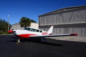 A white and red painted aircraft, N9338P, is parked on the tarmac in front of a hangar.