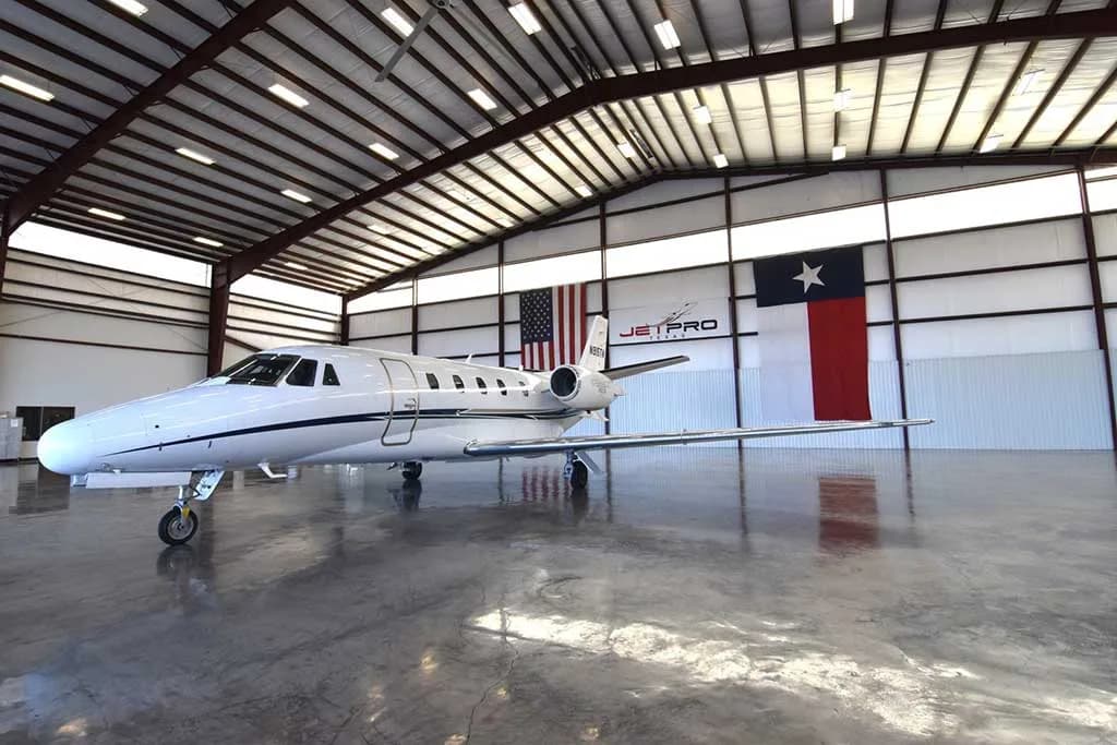 A white Cessna Citation XLS business jet with blue and silver stripes, tail number N915TM, parked inside a hangar.