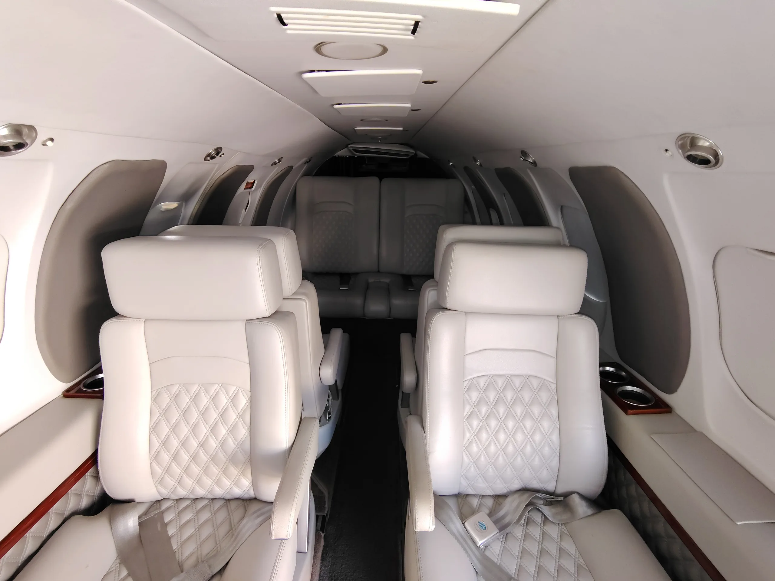 A view down the aircraft cabin aisle, showing rows of light gray quilted leather seats.