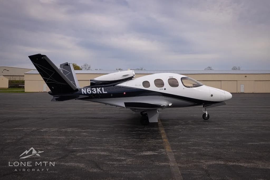 A side view of a white and black Cirrus Vision Jet (N63KL) parked on an asphalt apron.