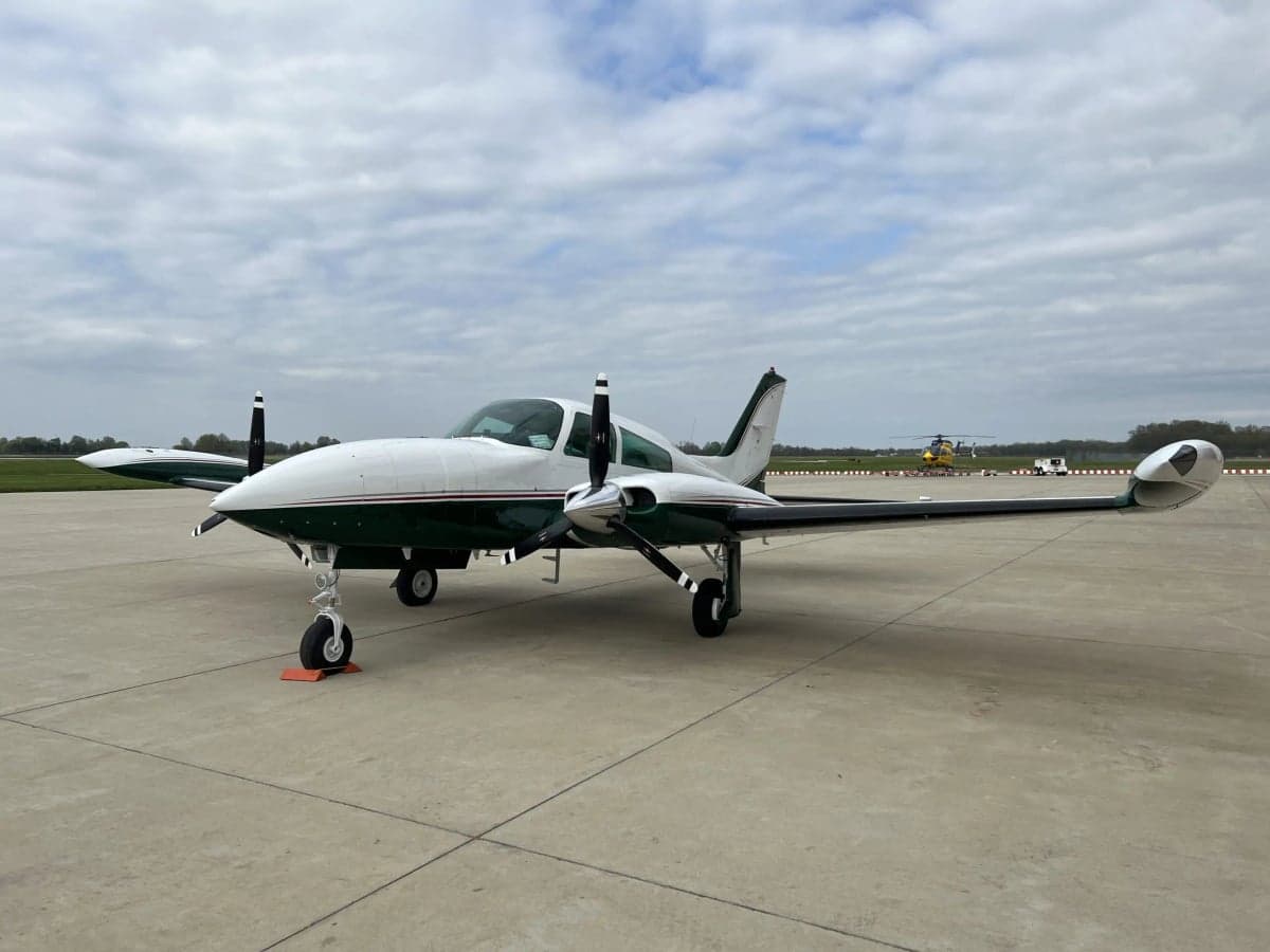 N4264J is a white and green Beechcraft Bonanza on the tarmac with a helicopter in the background.