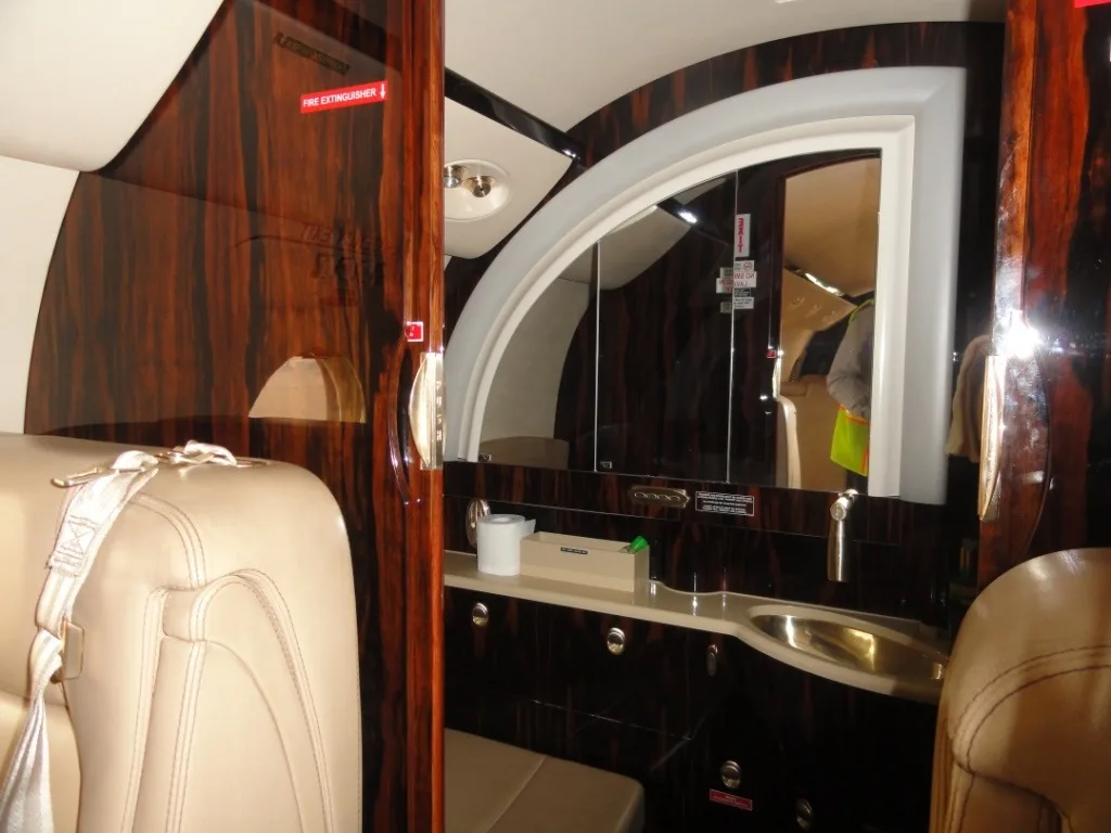A luxurious aircraft lavatory or galley area with dark wood paneling, a sink, and a large mirror.