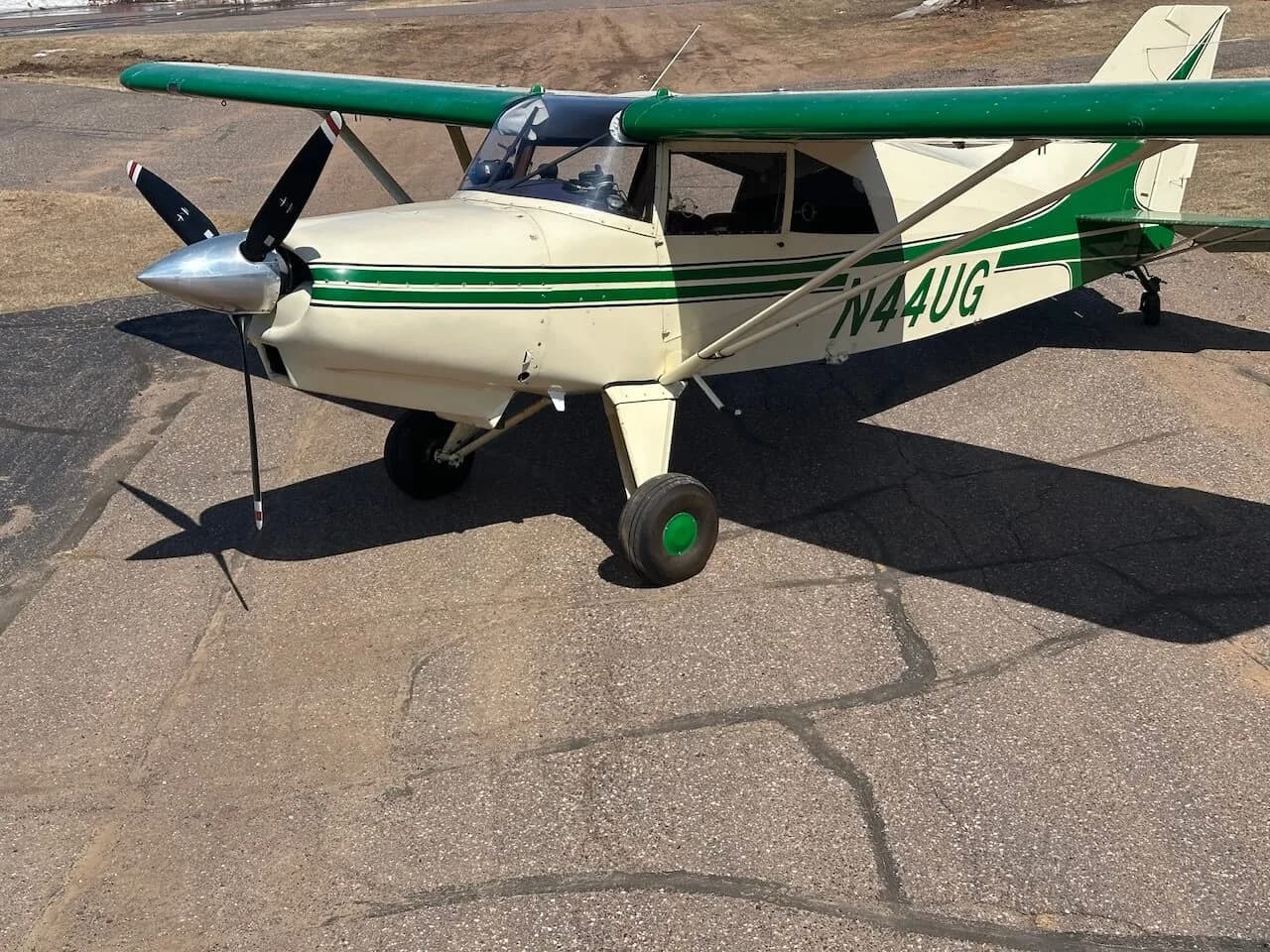 A front-side view of a Maule aircraft with a green and white paint scheme on an asphalt airfield.