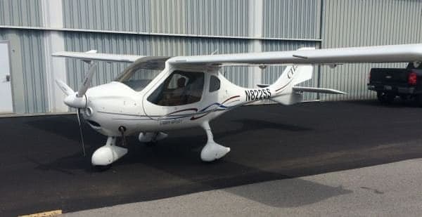 A white CTLS light sport aircraft is parked outside a hangar.