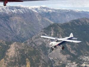 A Cubcrafters aircraft in flight over a mountainous landscape.