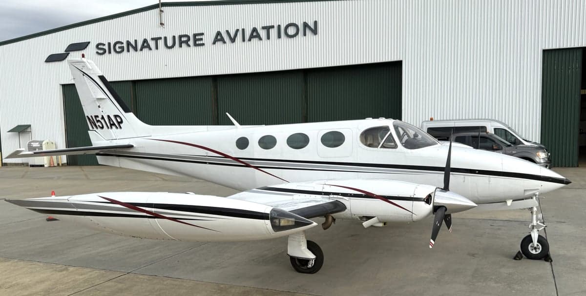Side view of the Cessna 340A aircraft with registration N51AP parked in front of a Signature Aviation hangar.