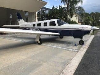 A white and blue Piper Saratoga II HP is parked outside a building.