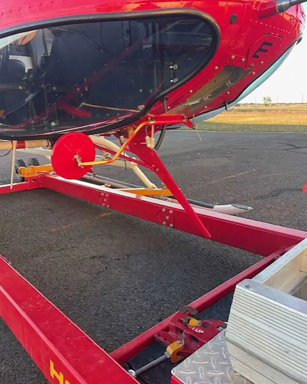 A close-up view of the red helicopter's tail boom and a red ground handling cart on an asphalt surface.