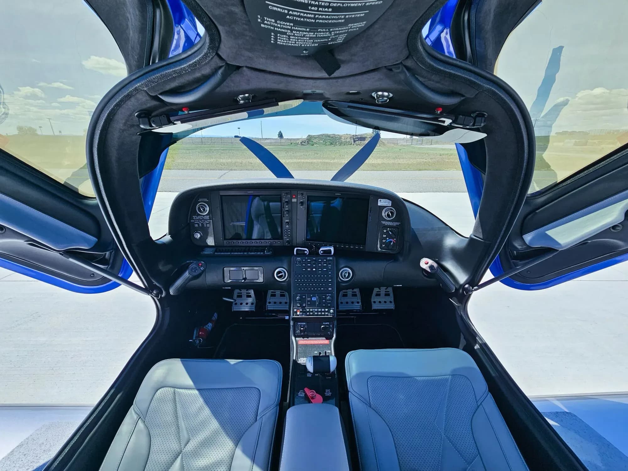 A wide view of the Cirrus SR22T cockpit with dual Garmin screens, light blue seats, and open gull-wing doors.