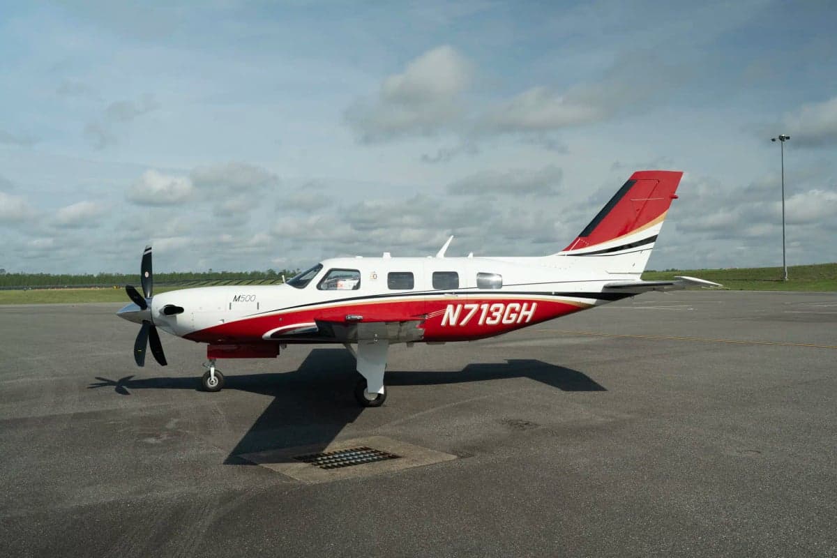 A white and red Piper M500 aircraft with registration N713GH parked on an asphalt tarmac under a partly cloudy sky.