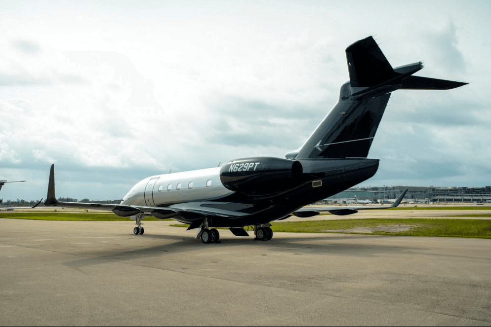 The rear view of a silver and dark blue Embraer Legacy 600 private jet, tail number N629PT, parked on an airfield under a cloudy sky.