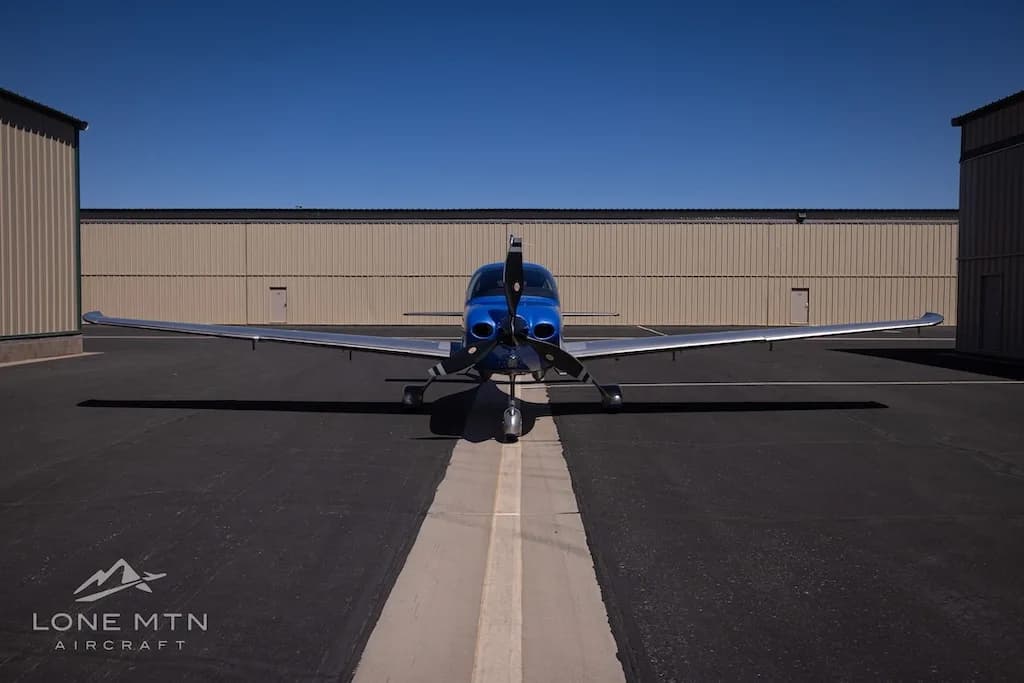A head-on view of the blue and silver Cirrus SR22 aircraft, N365S, parked on an asphalt ramp between hangars.