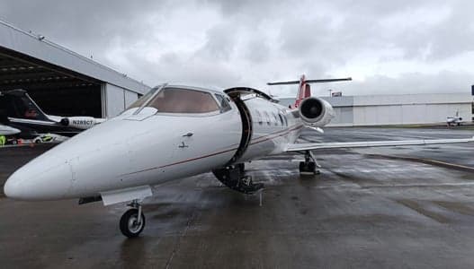 A Learjet aircraft is parked on the tarmac with its door open.