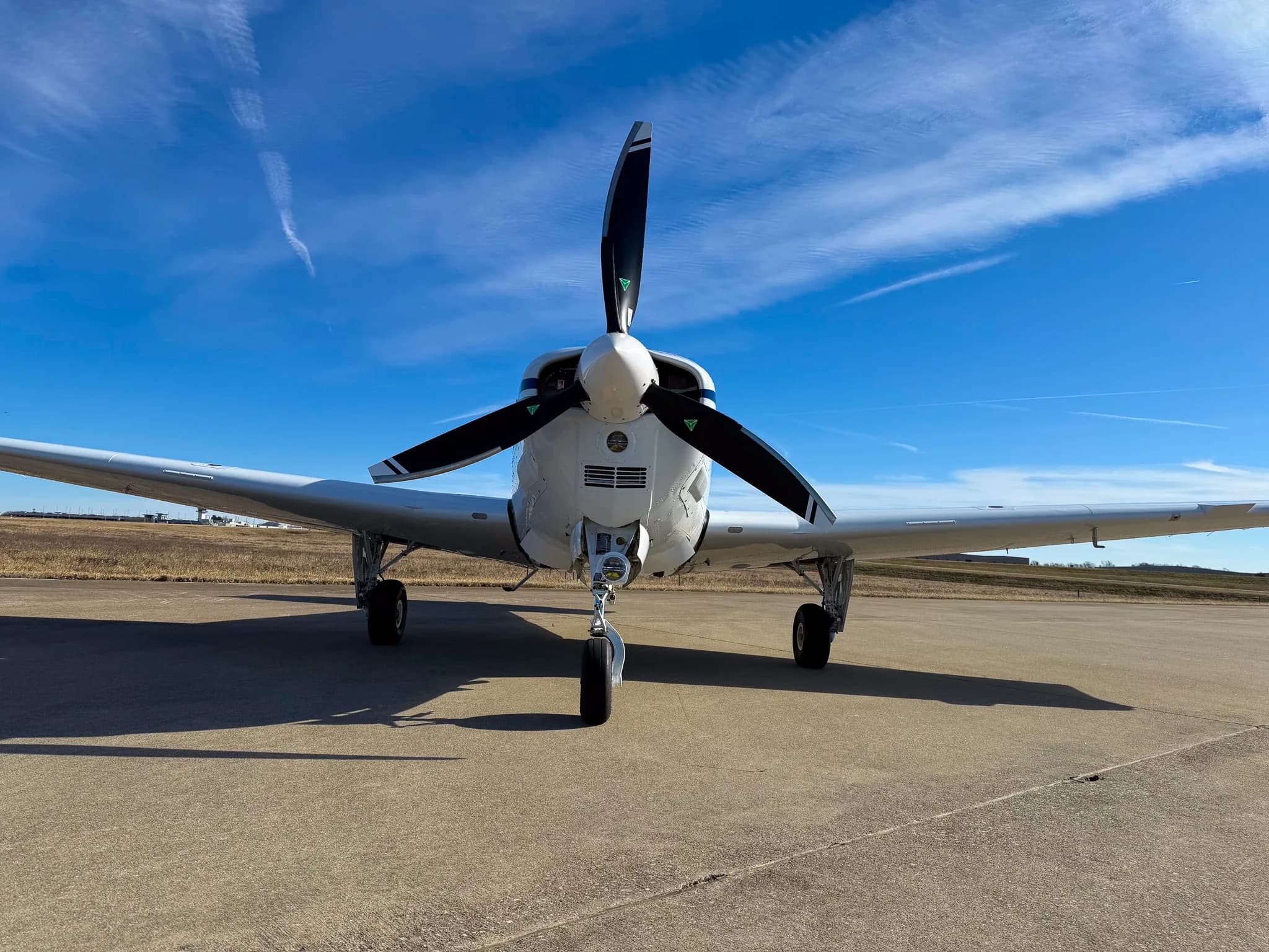 A head-on view of a white Beechcraft Bonanza G36 with its propeller, registration N7CM, parked on an airfield.