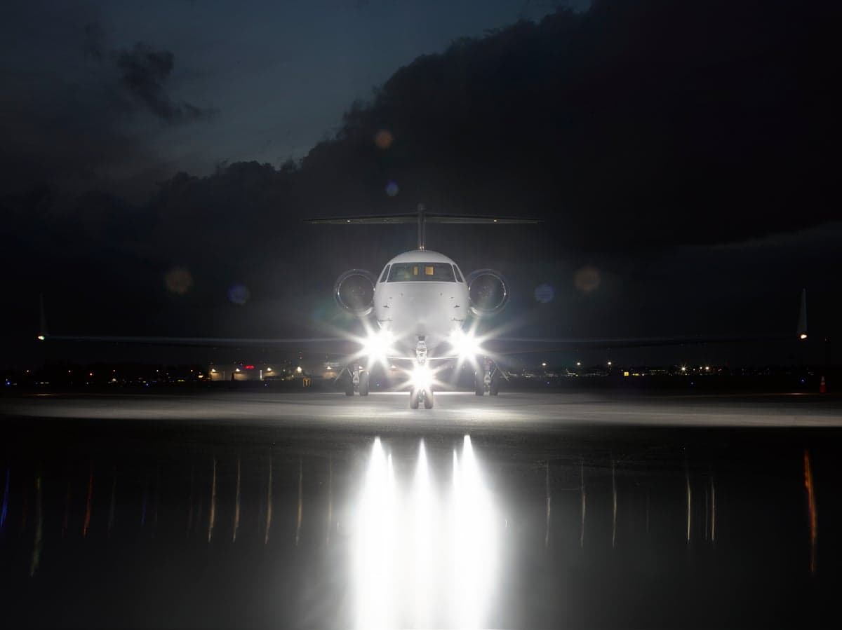 Front view of the aircraft on the tarmac at night with its landing lights on.
