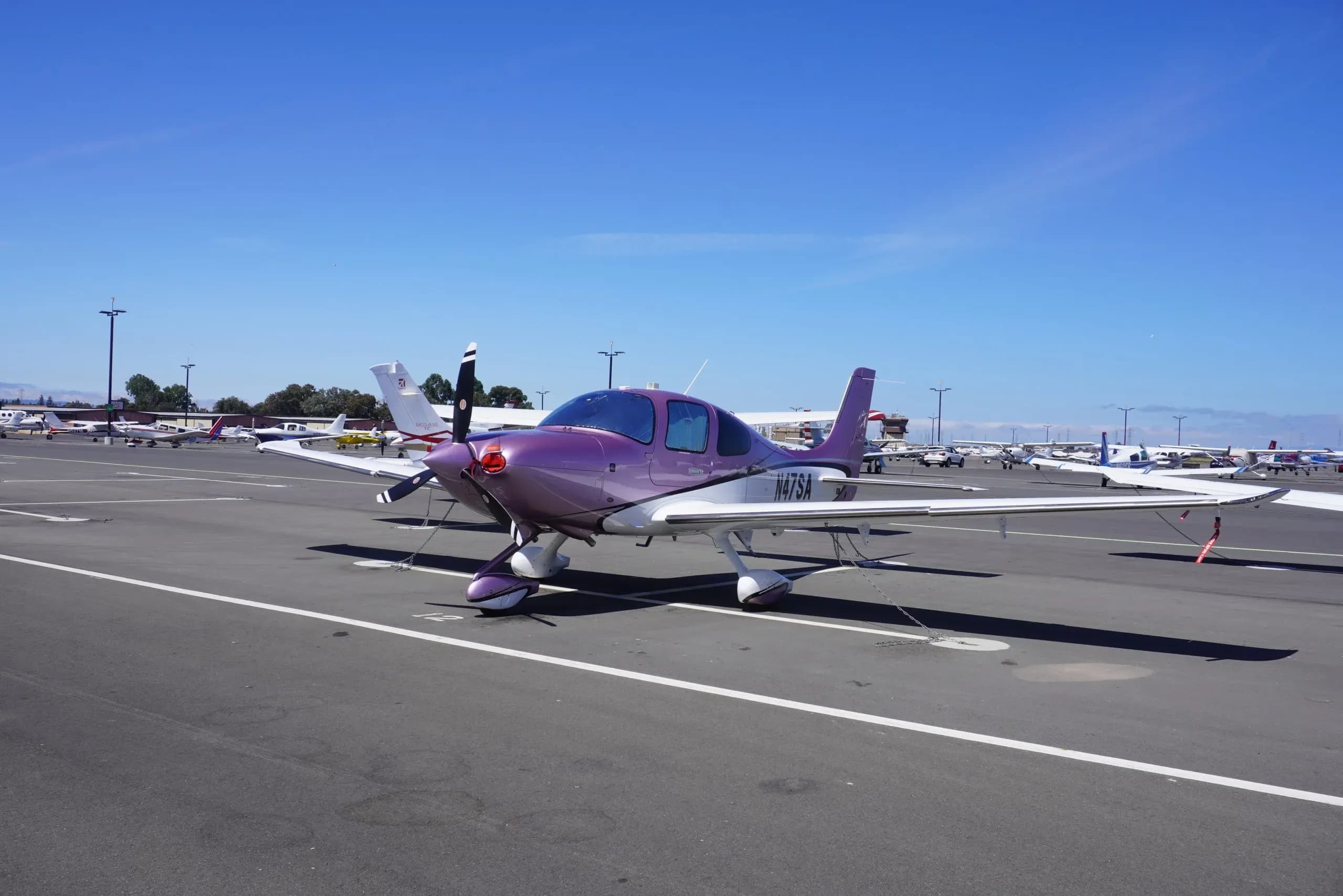 A Cirrus SR22 aircraft with a purple paint scheme is parked on the tarmac.