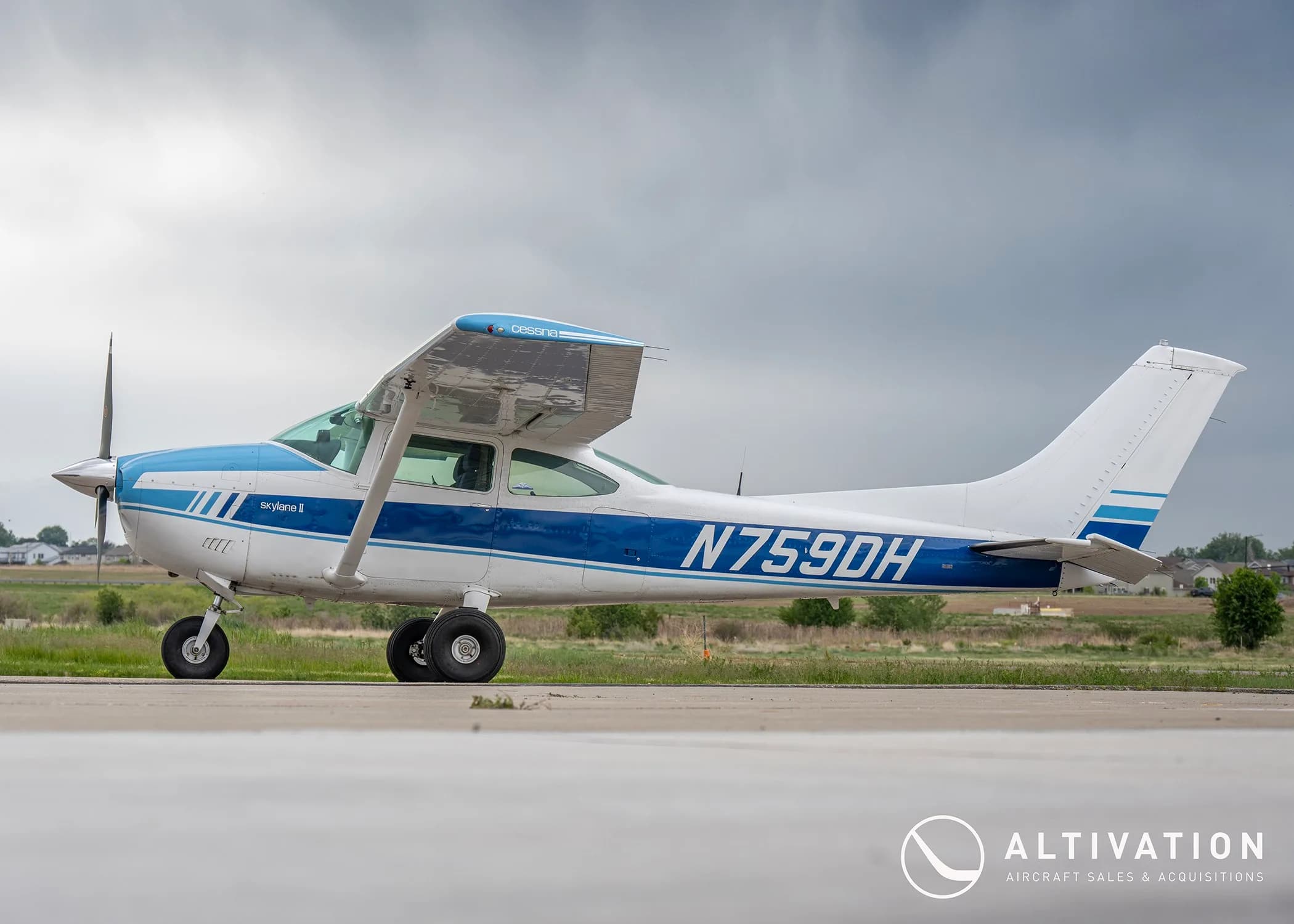 A side view of a white and blue Cessna 182 Skylane II (N759DH) parked on an airfield.