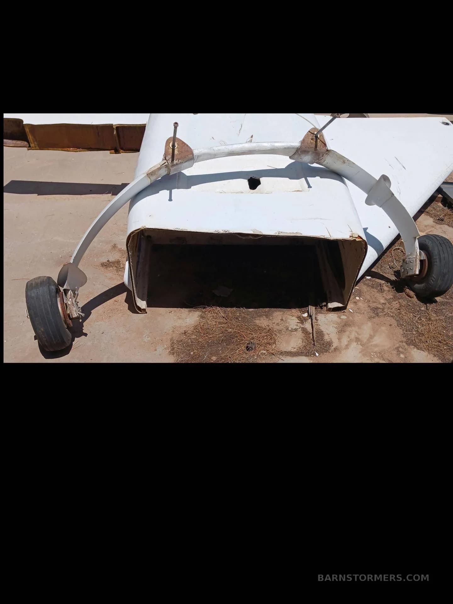 A white aircraft fuselage section with a bent landing gear assembly and wheels lies on dry ground.
