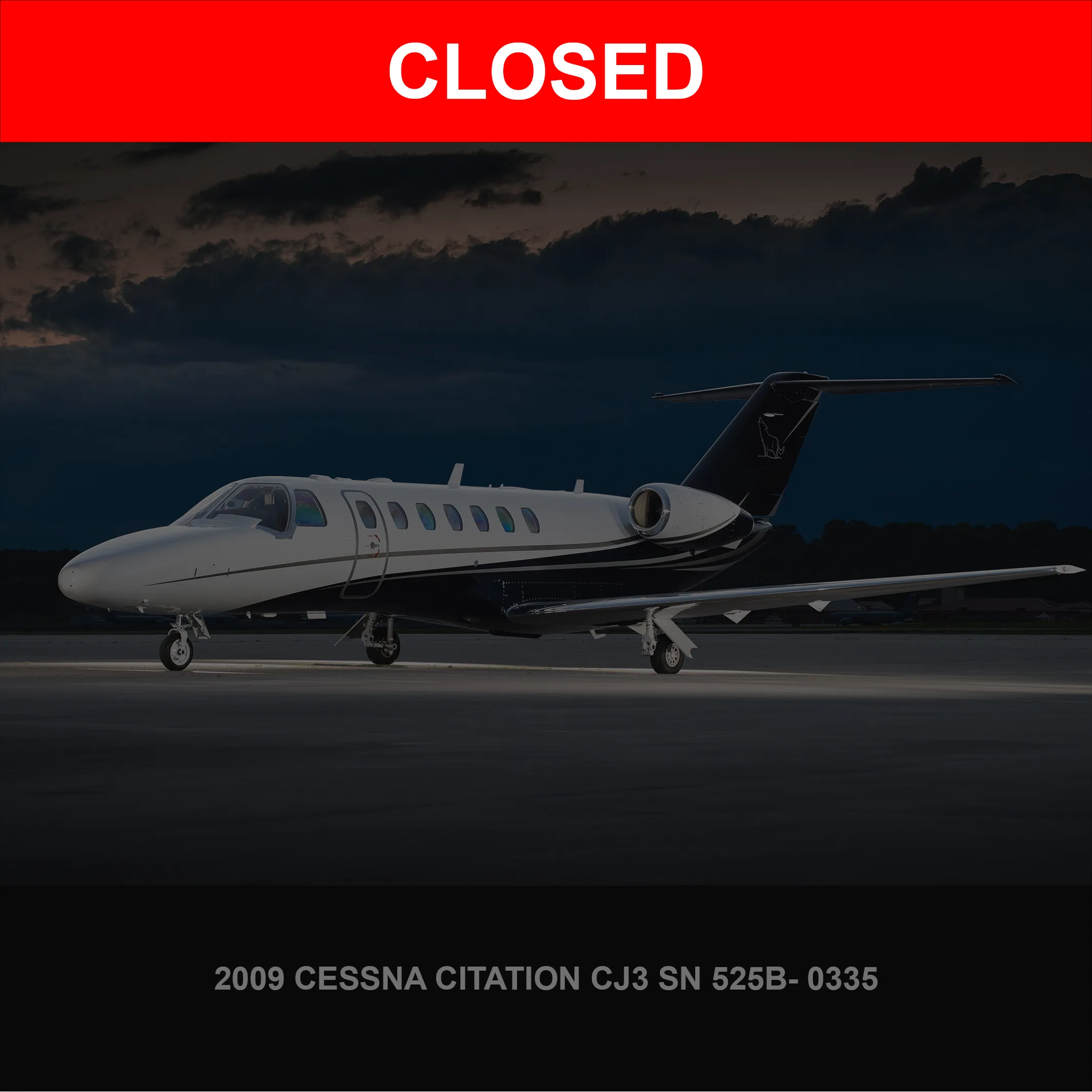 A white and black Cessna Citation CJ3 business jet is parked on a tarmac at dusk, lit from below.