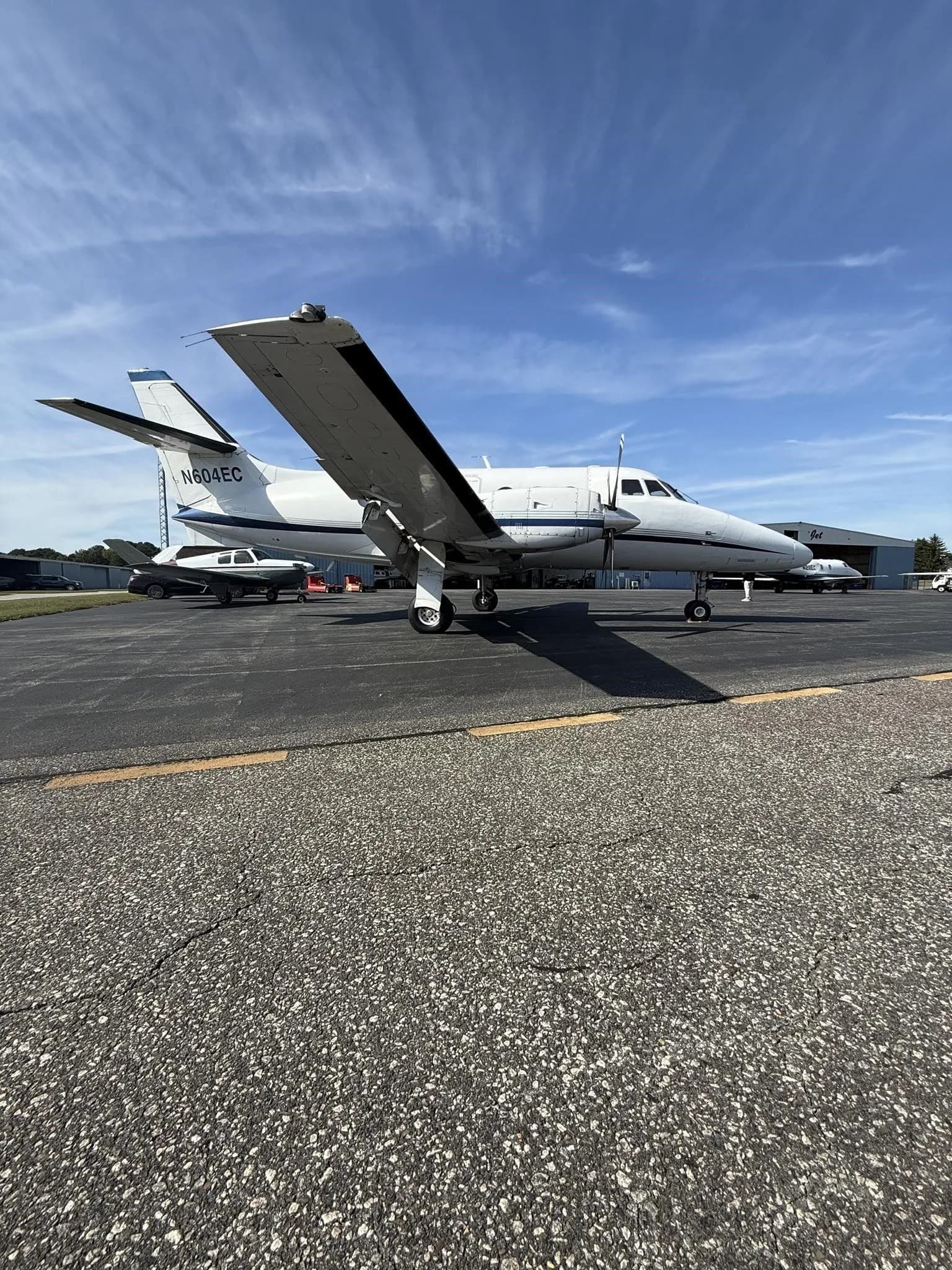 A low-angle side view of a white Jetstream 31 aircraft with blue accents, tail number N604EC, parked on an asphalt tarmac.