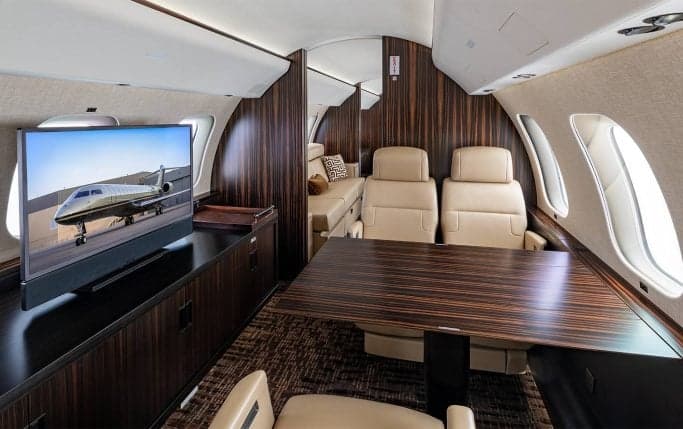 Aircraft interior with leather seats and a monitor displaying an aircraft image.