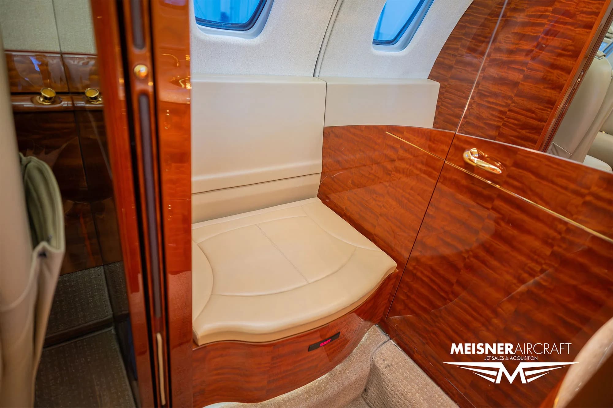 A close-up view of a beige leather bench seat and polished wood paneling inside a business jet cabin.
