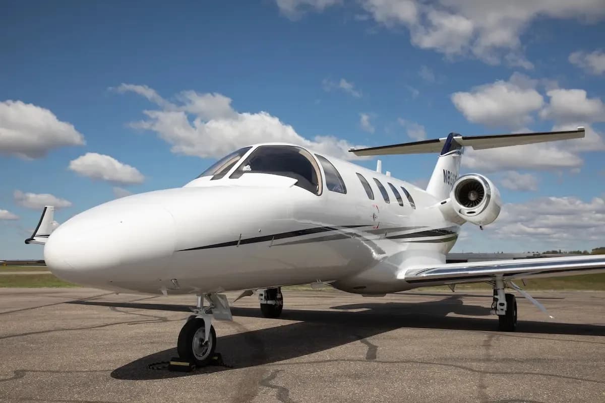 A front-side view of a white Cessna Citation CJ1+ (N868AC) with blue and grey stripes on an airfield.