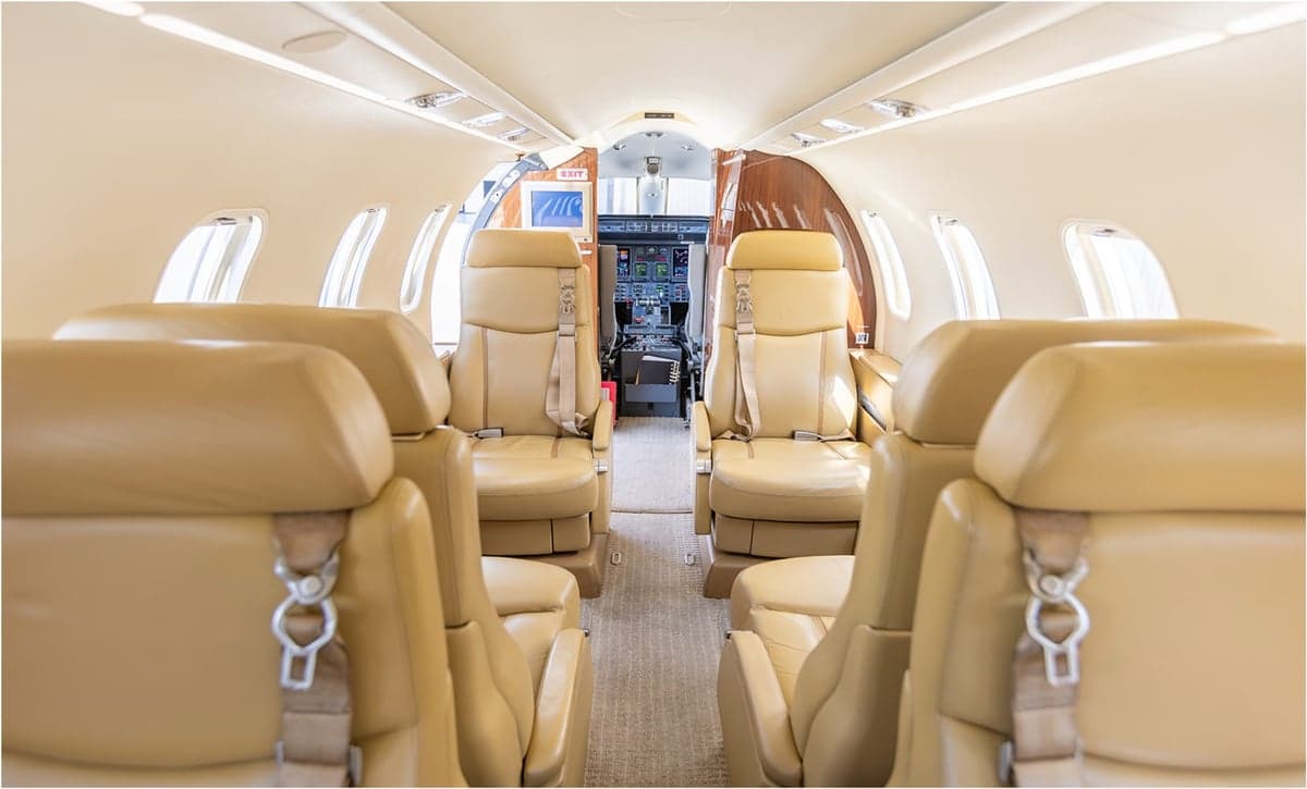 The interior cabin of an aircraft with tan leather seats and a view towards the cockpit.