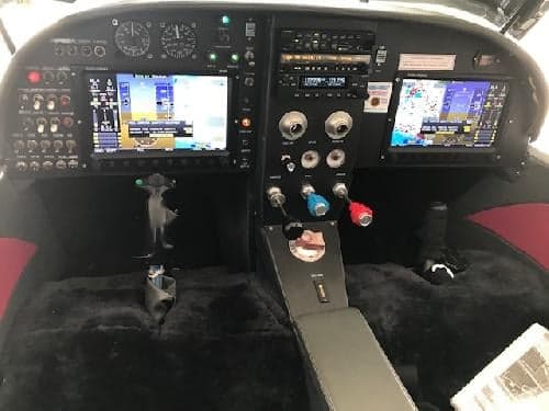 The cockpit of an aircraft features a black instrument panel with multiple screens and controls.