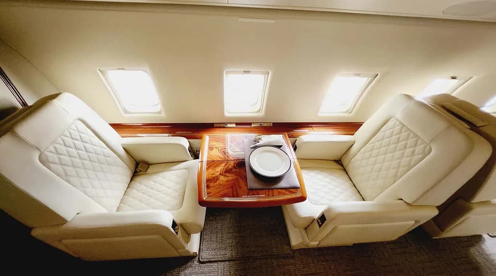 A close-up view of two cream quilted leather seats facing each other, separated by a polished wooden table with a plate.