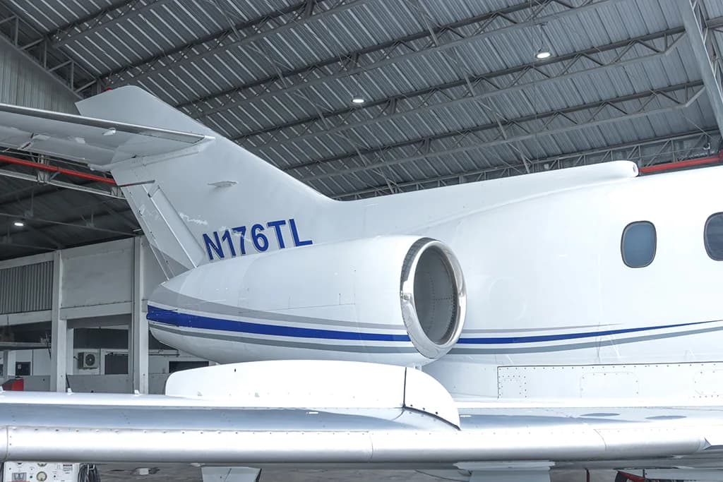 A close-up of the tail section of a white business jet with blue and grey stripes, showing registration N176TL.