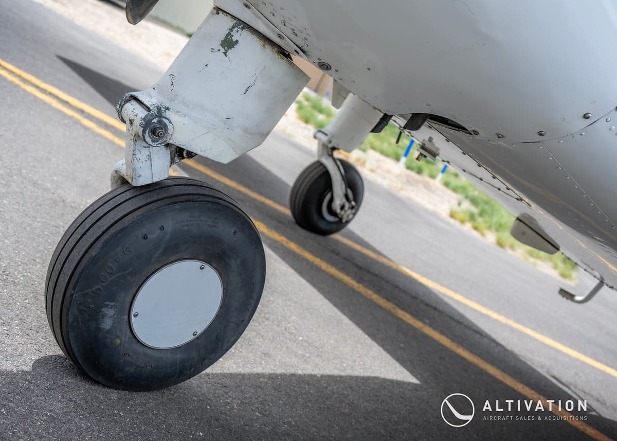 Close up of the landing gear of a white and blue Piper aircraft.