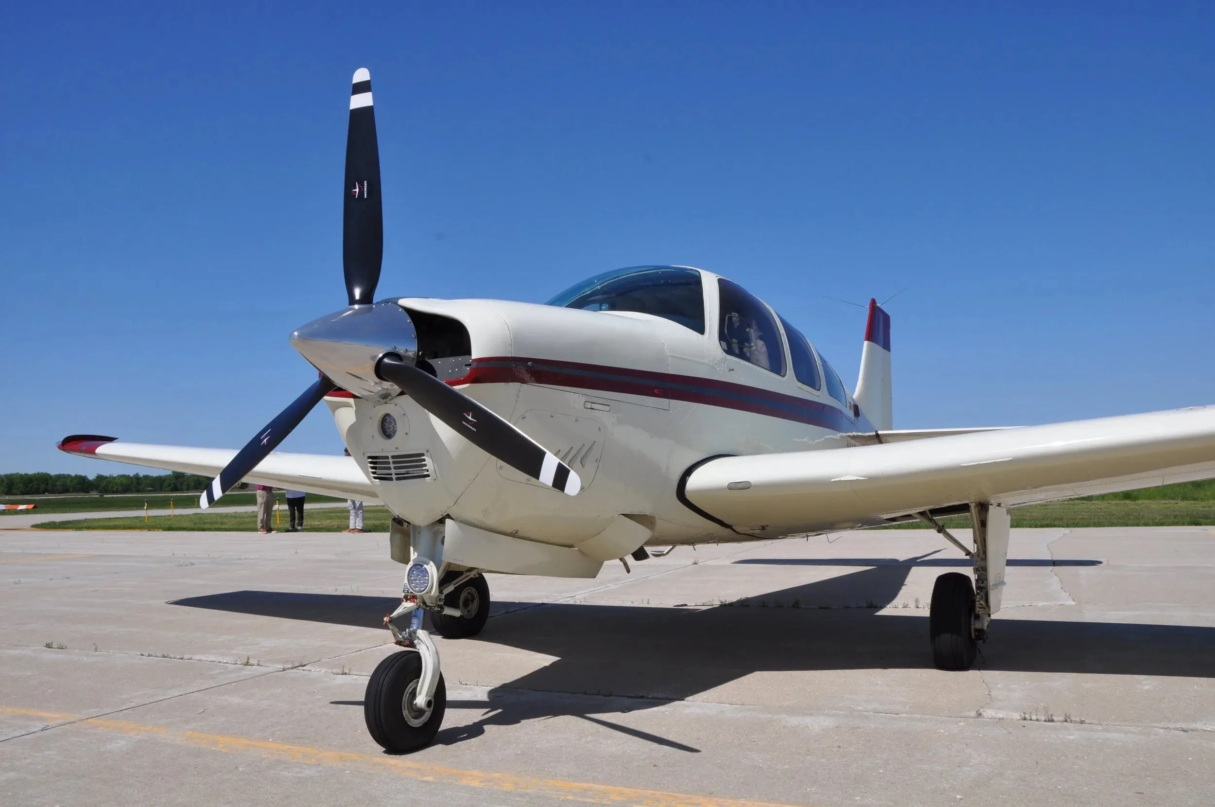 A close-up front view of the white and maroon Beechcraft Bonanza F33A N159GM on a tarmac.