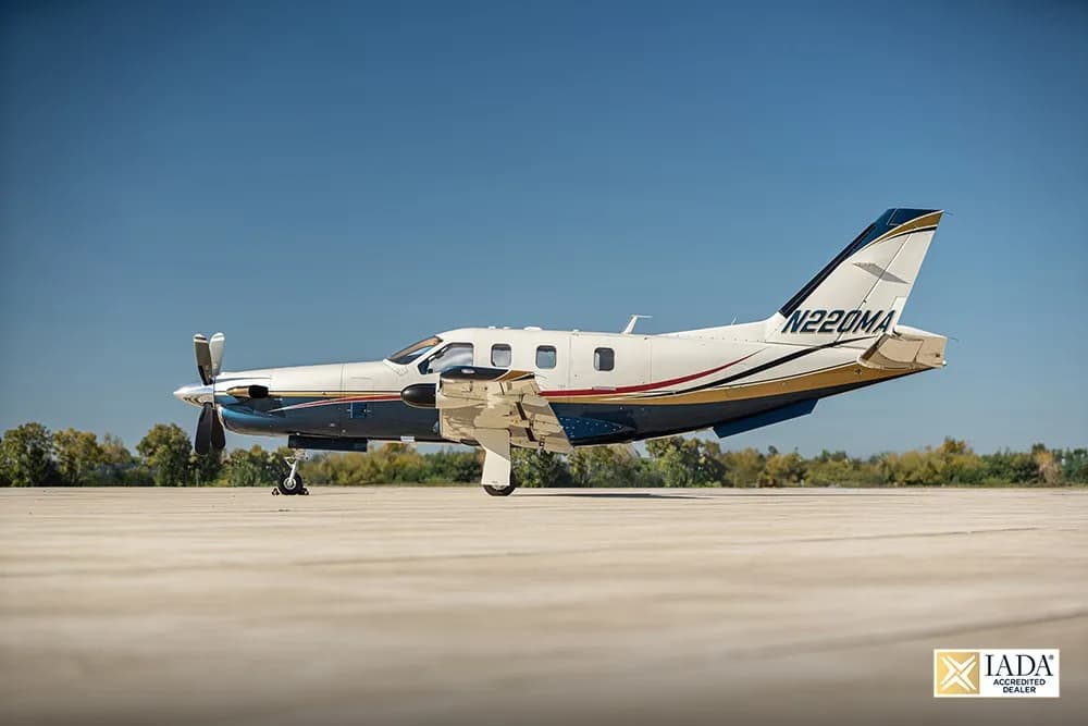A white, blue, and gold painted turboprop aircraft (N220MA) parked on an airfield, viewed from the side.