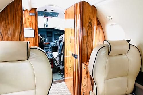 The aircraft's interior shows cream-colored leather seats and a view into the cockpit.