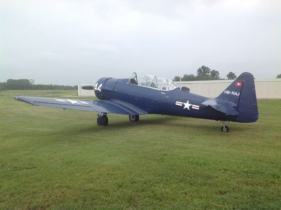 A blue North American T-6 Texan aircraft parked on a grassy field.