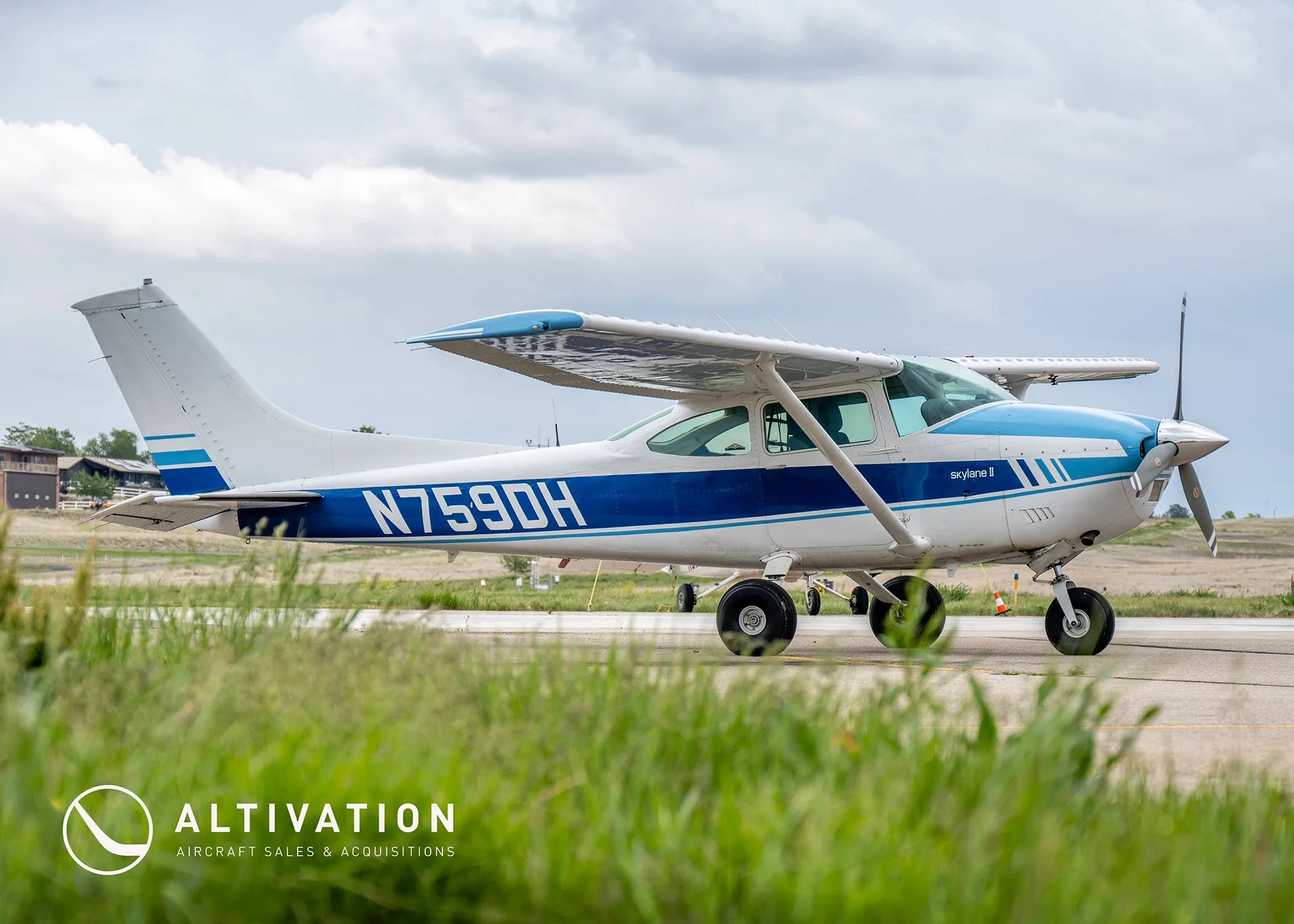 A low-angle side view of a white and blue Cessna 182 Skylane II (N759DH) on an airfield.