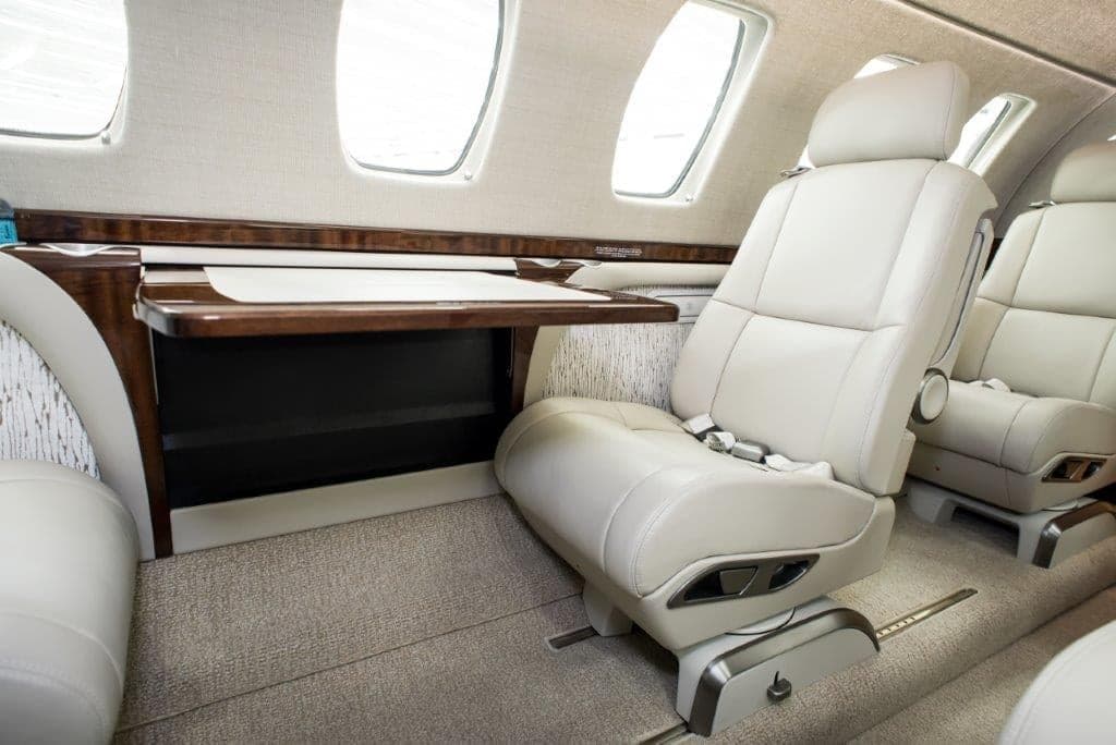A close-up view of a light-colored leather passenger seat and a wooden fold-out table in the aircraft cabin.