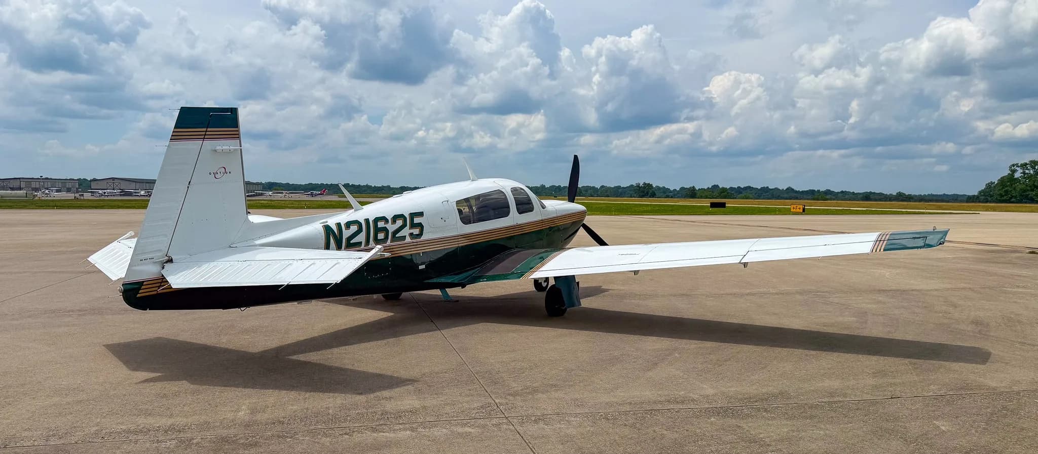 A rear-side view of the white and green Mooney M20 aircraft with registration N21625 on an airfield.