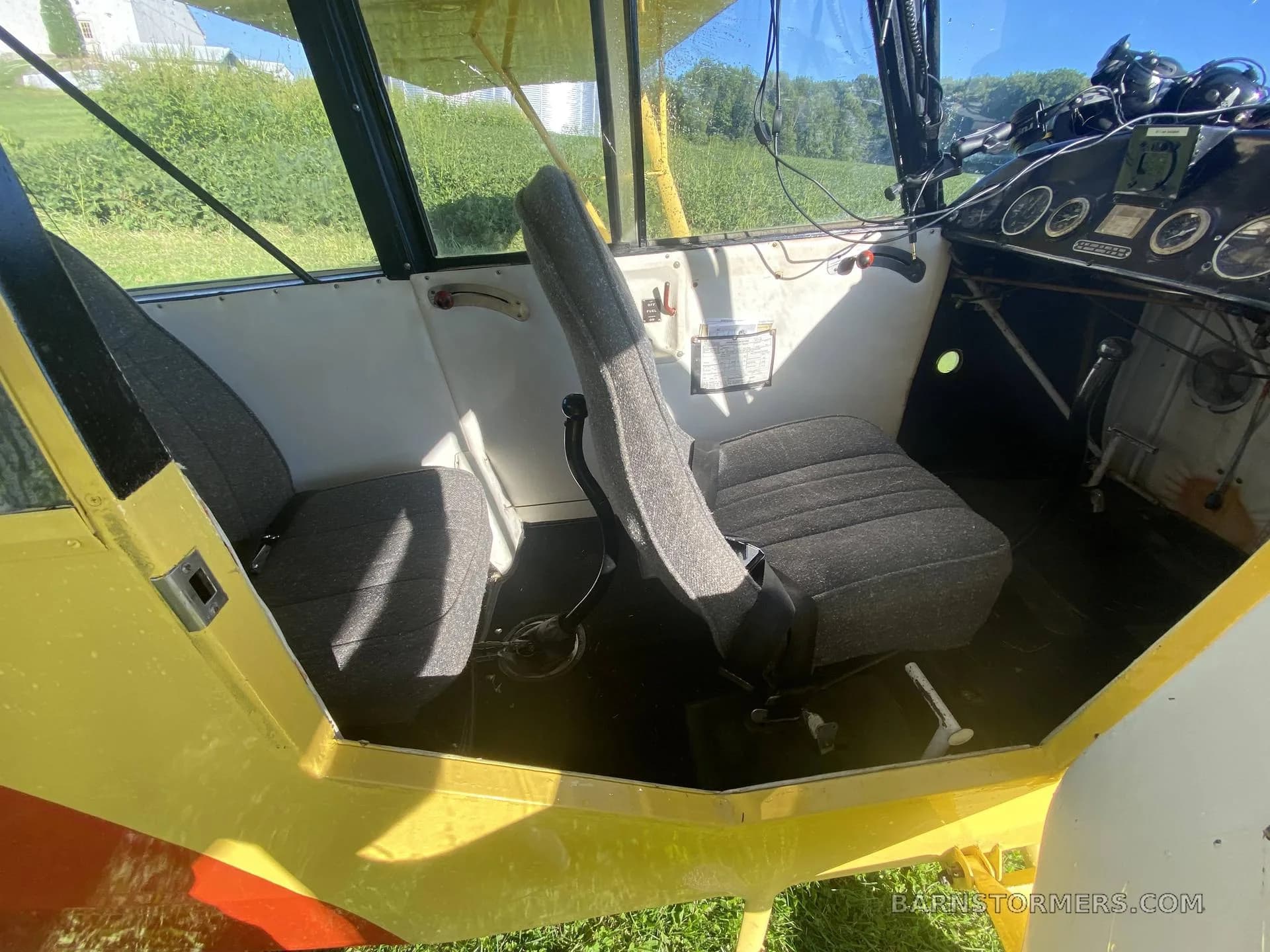 The interior of a small aircraft shows two grey fabric seats and a basic instrument panel on the right.