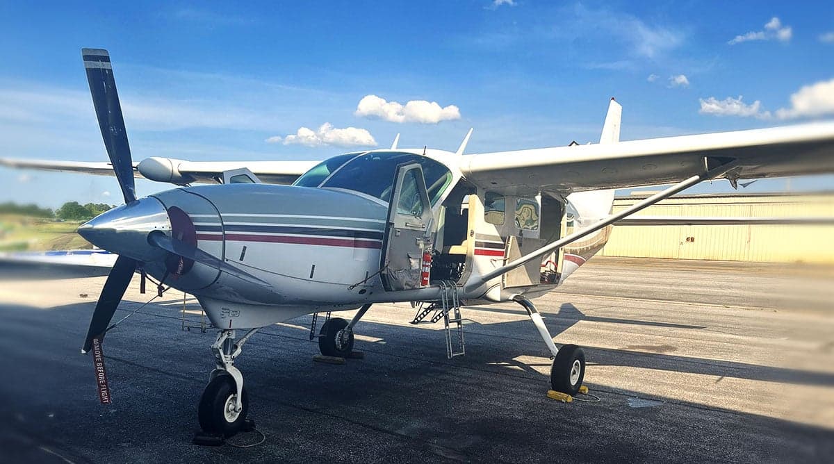 Front side view of a silver and white Cessna 208 Caravan with the door open.