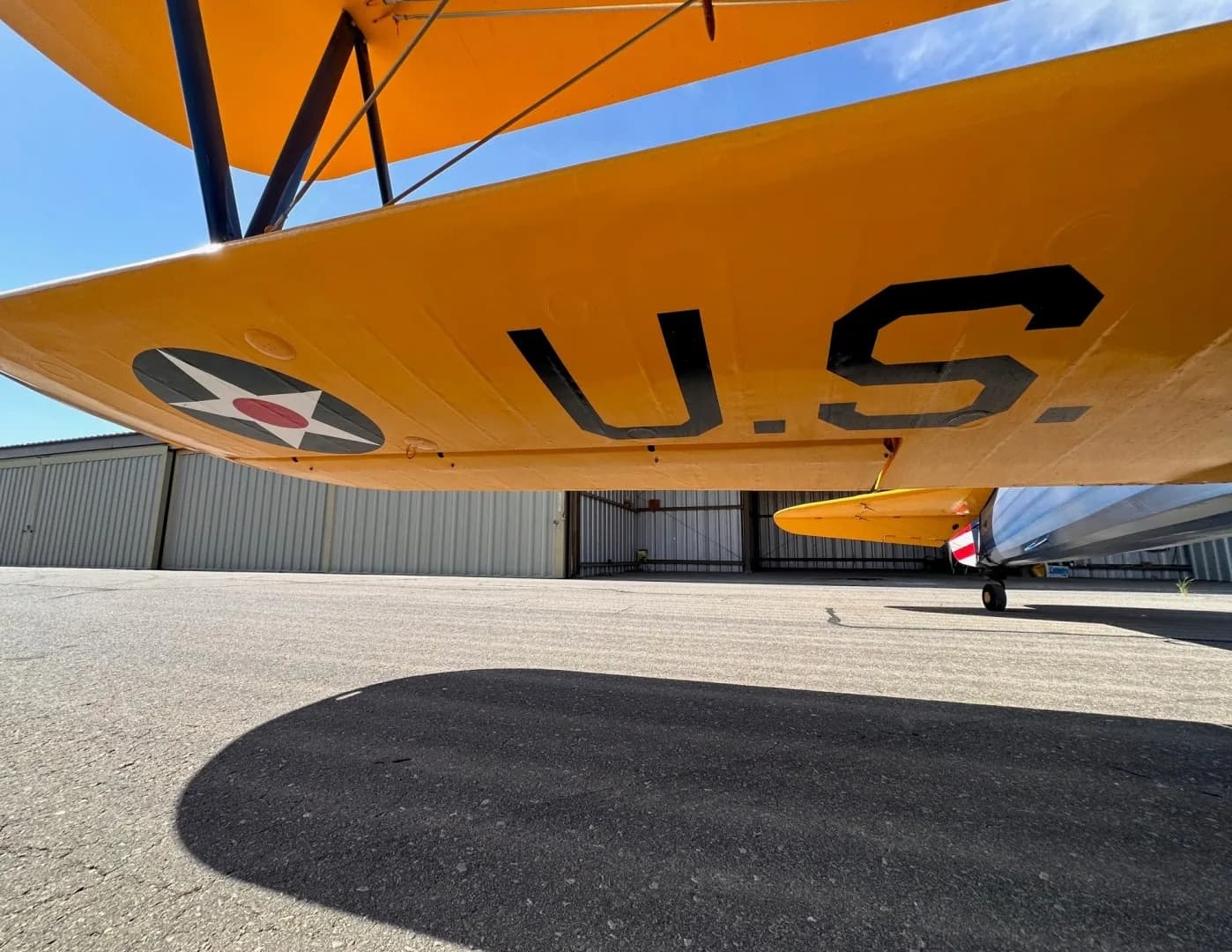 A close-up view of the underside of a yellow biplane wing, showing "U.S." text and a US military star insignia.