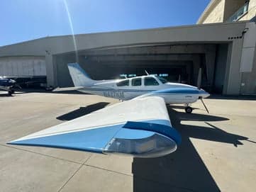 A Beechcraft Bonanza with blue and white paint scheme is parked on the tarmac.