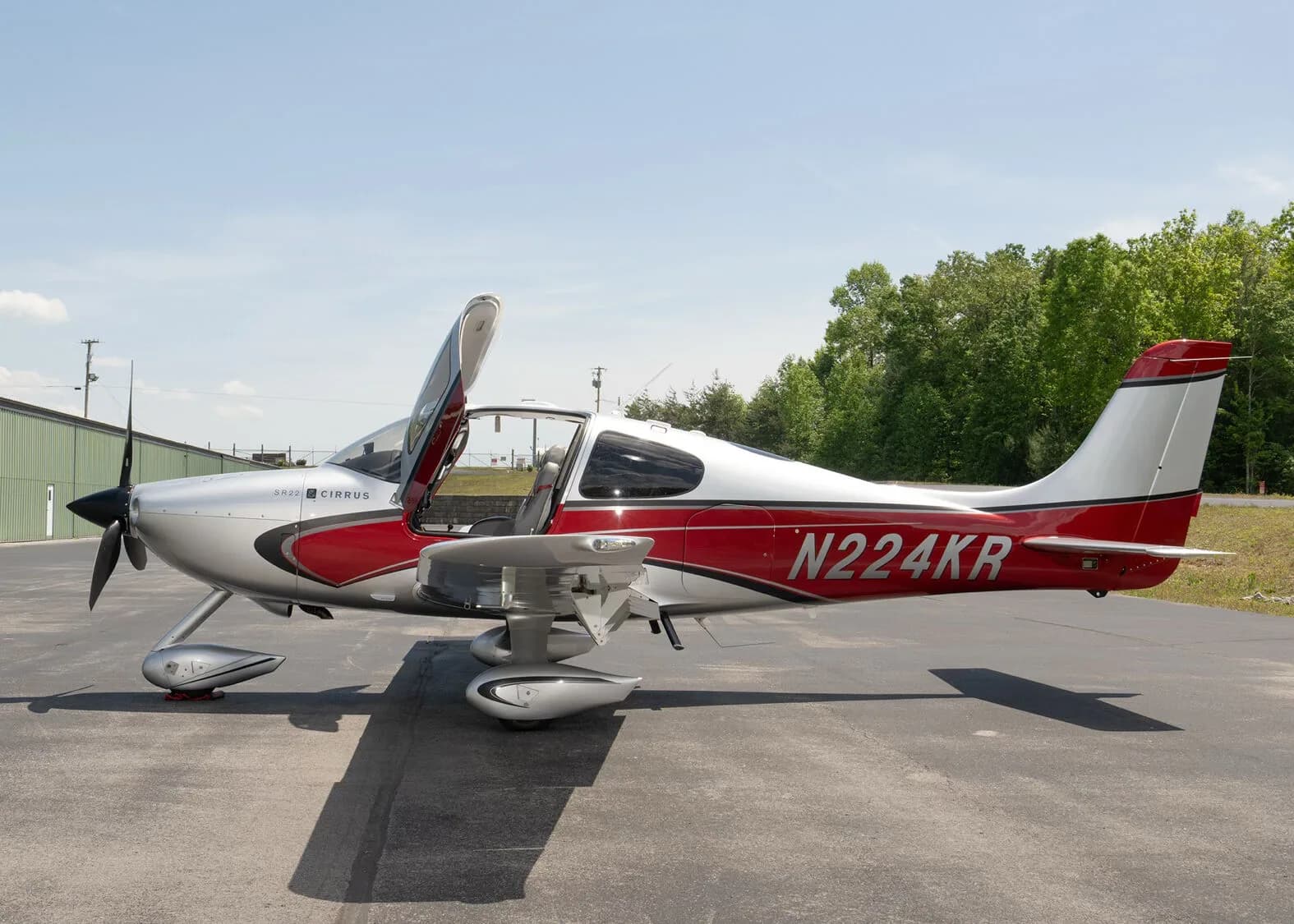 A silver and red Cirrus SR22 aircraft, N224KR, with its left gull-wing door open, parked on an asphalt ramp.