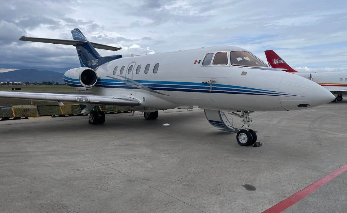 A white business jet with blue stripes (XB-OAE) parked on a tarmac, showing the front and right side.