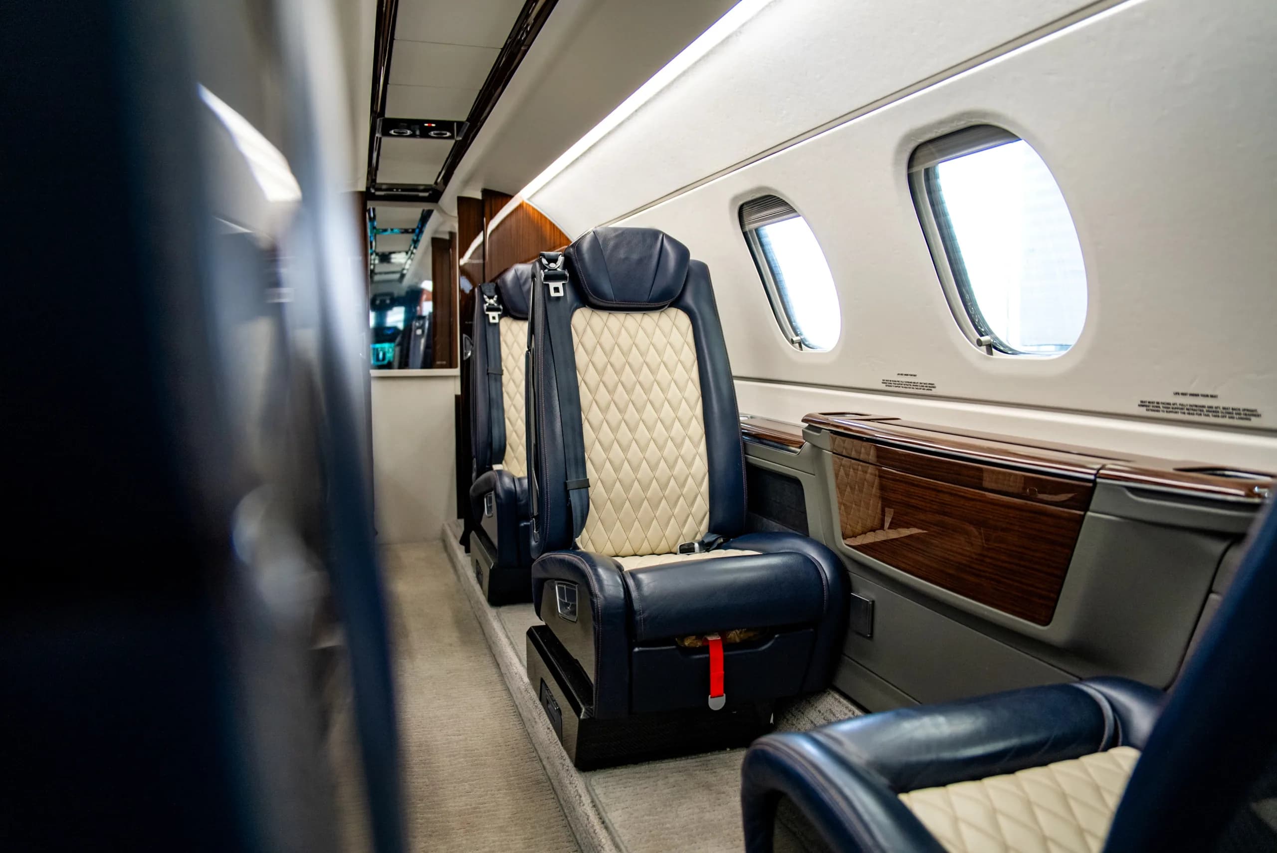 The luxurious cabin interior of an Embraer Phenom 300E, featuring dark blue and cream quilted leather seats.