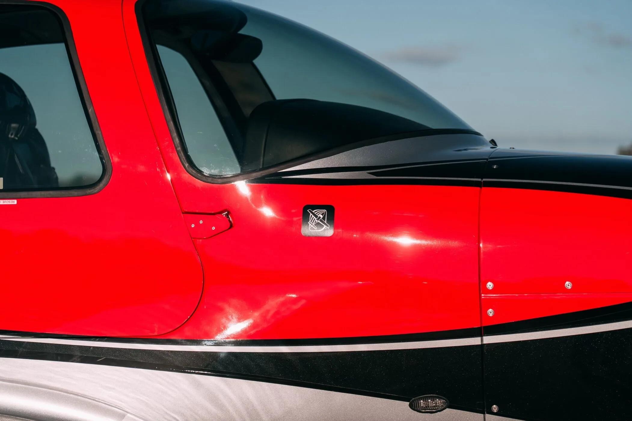 A close-up of the red, black, and silver fuselage of the Cirrus SR22T aircraft, showing a small emblem.