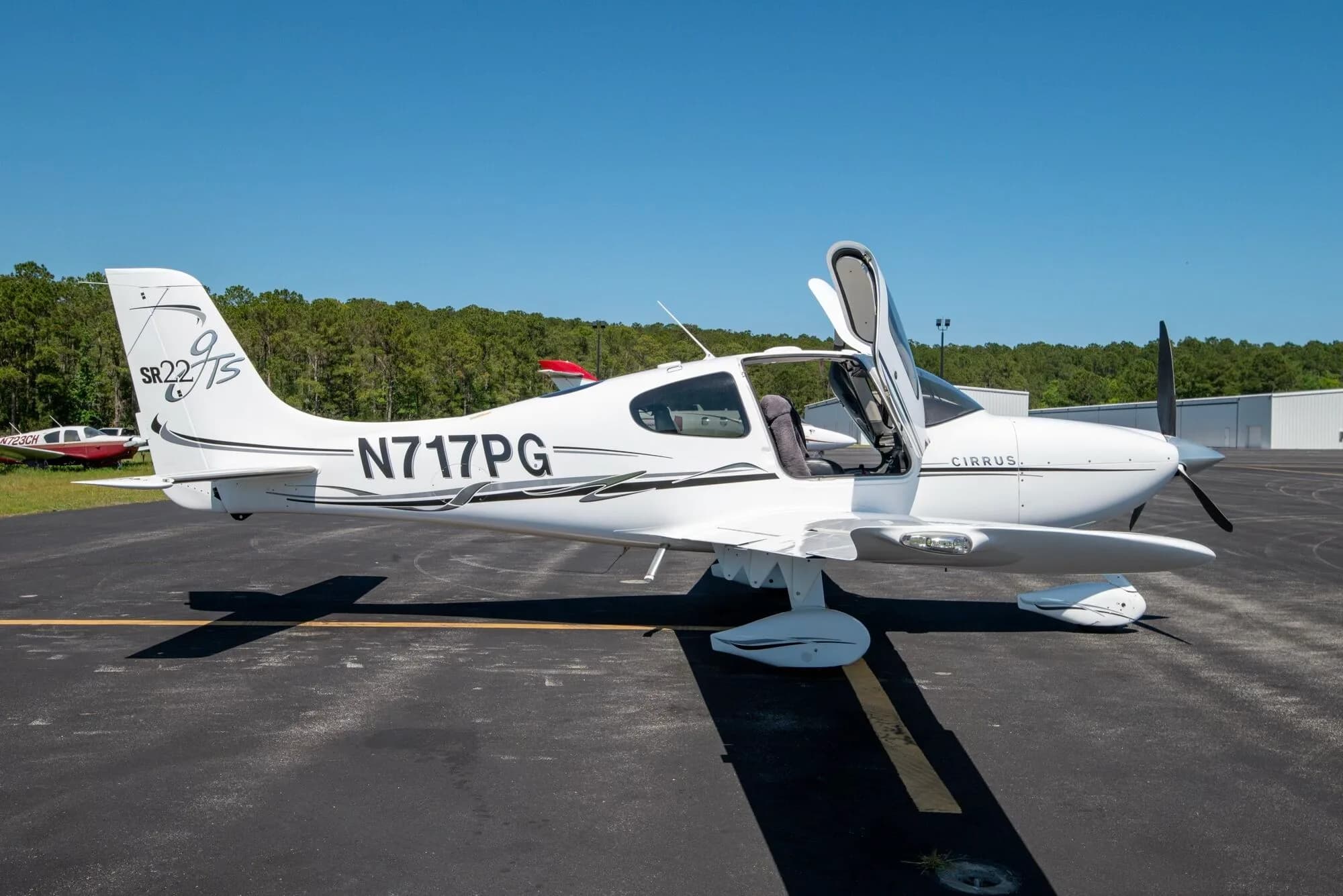 White Cirrus SR22T aircraft N717PG with black and grey stripes and open doors parked on an airfield.