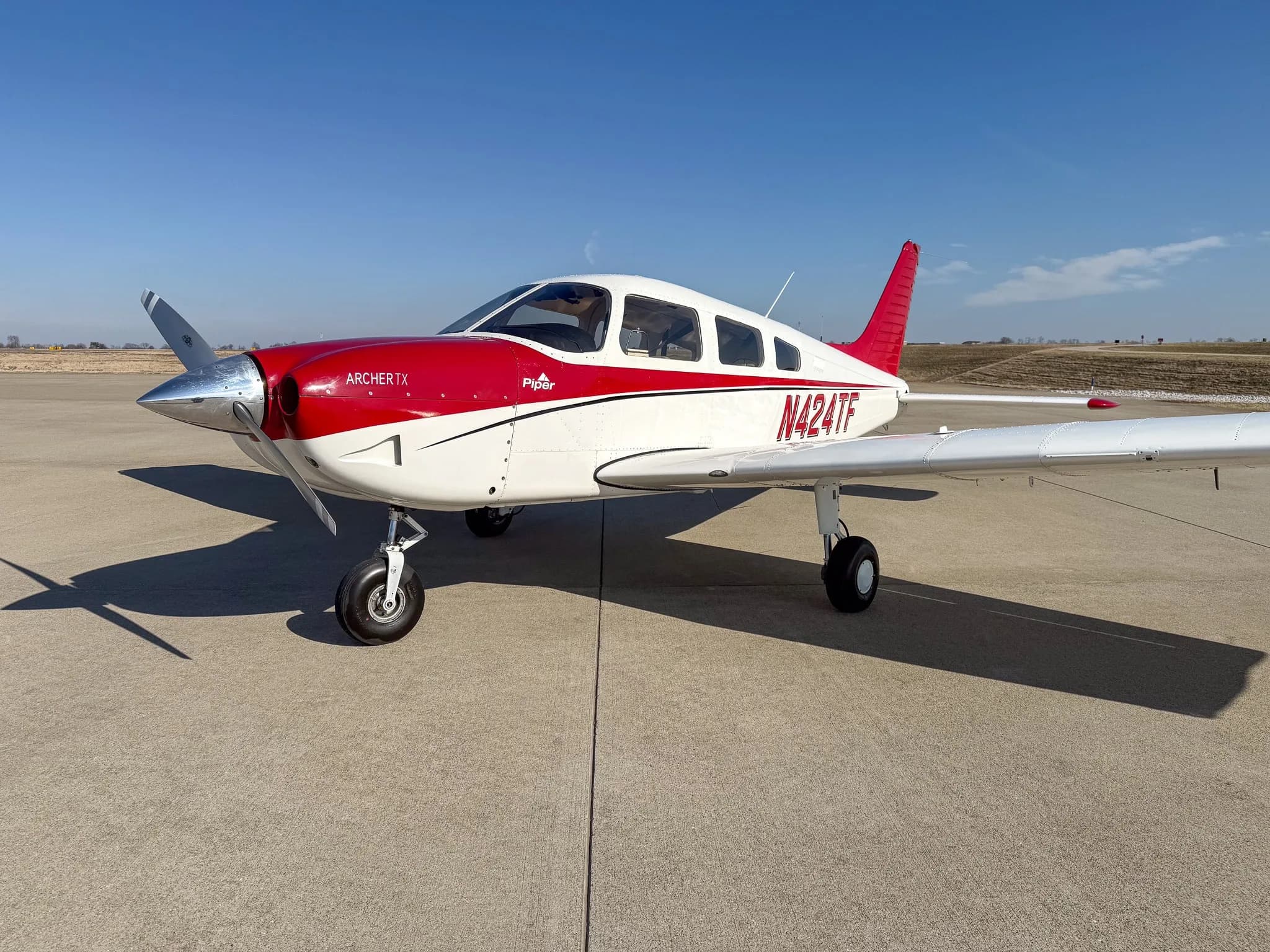 A white Piper Archer TX with red accents and tail number N424TF parked on an airfield under a clear blue sky.