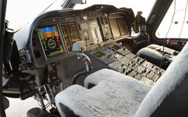 The instrument panel and seats of a helicopter cockpit.